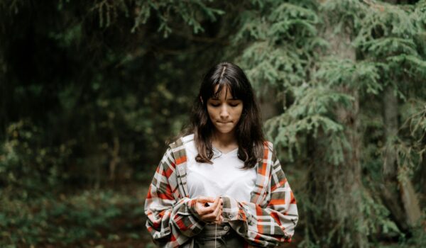 A teen sitting quietly outdoors, eyes closed, practicing mindfulness to reduce stress and anxiety.
