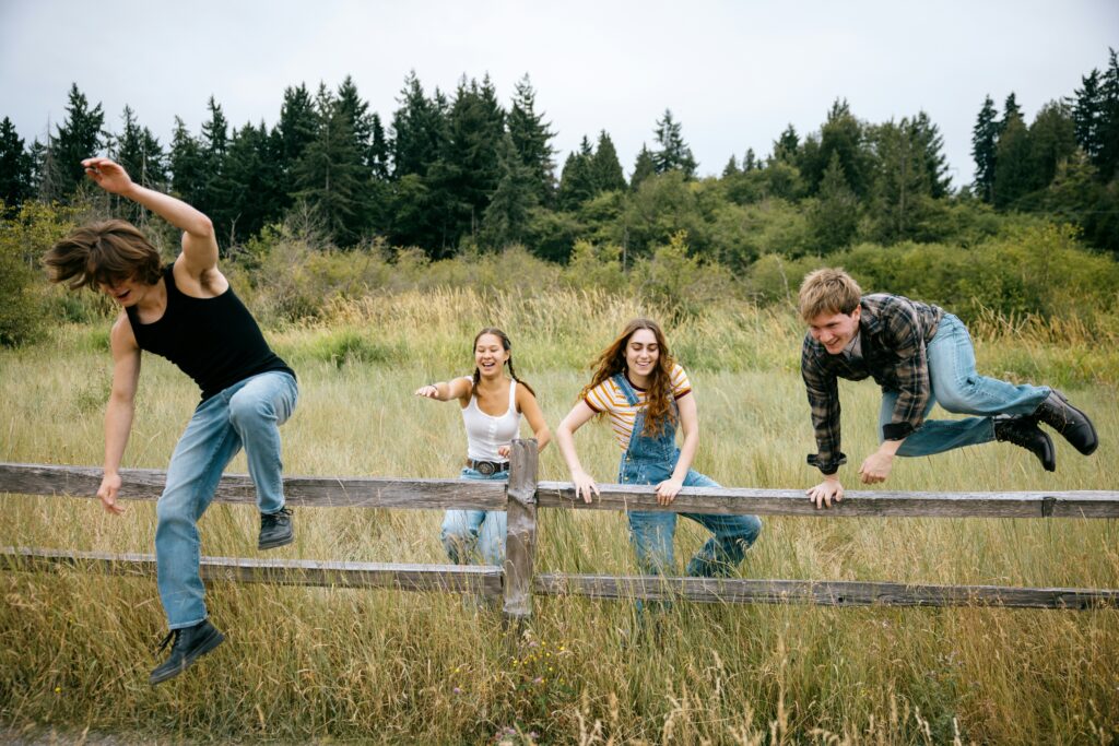 Group of teens jumping over a wooden fence in a field, representing friendship, social connection, and student life balance.