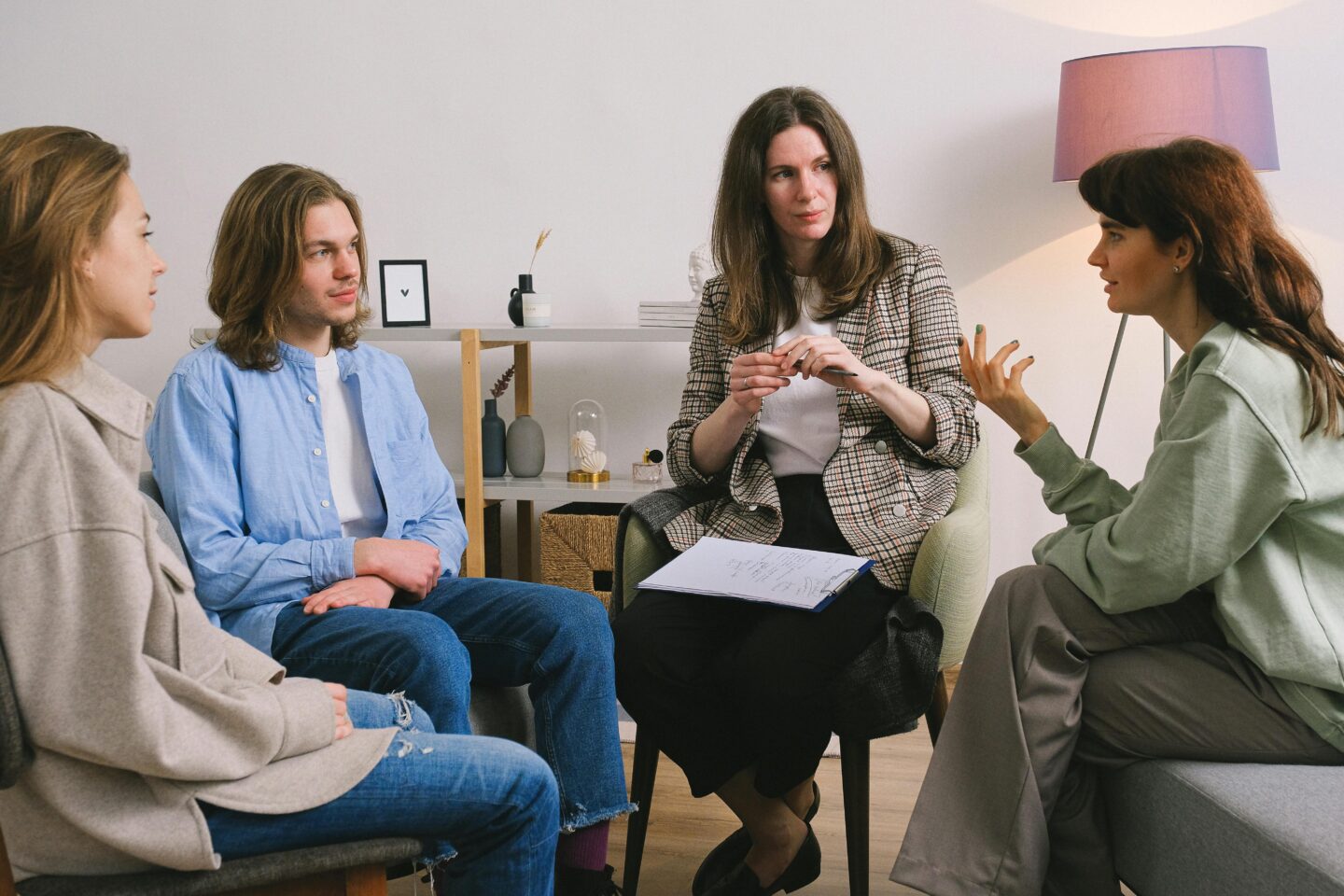 Teenagers participating in a school group therapy session with a school counselor, sitting in a circle and actively listening and sharing in a calm, supportive environment.