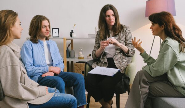 Teenagers participating in a school group therapy session with a school counselor, sitting in a circle and actively listening and sharing in a calm, supportive environment.