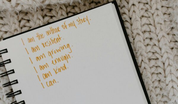 A spiral notebook with handwritten affirmations in gold ink reading 