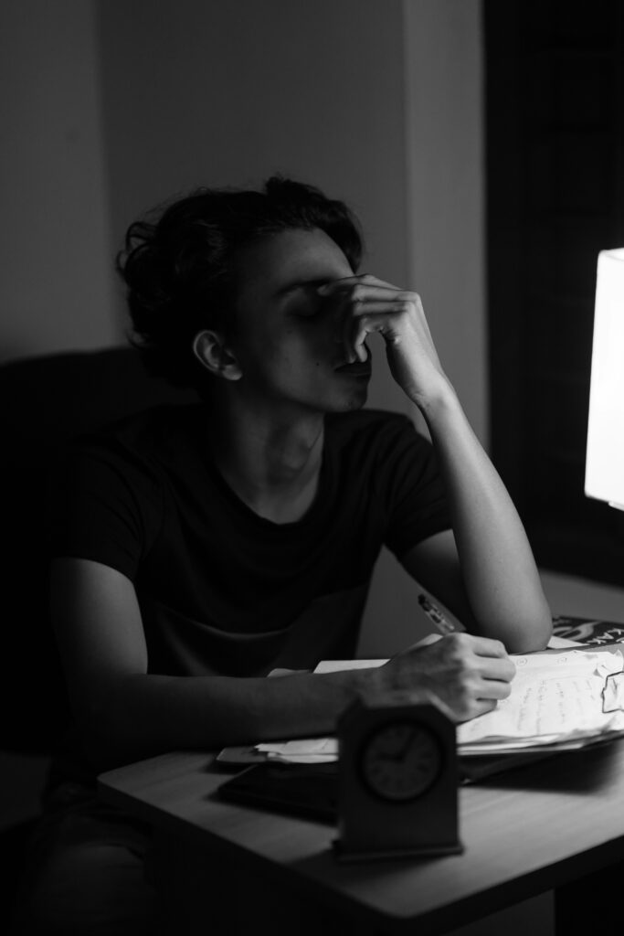 Teen student sitting with homework looking stressed about mental health and academic pressure. 