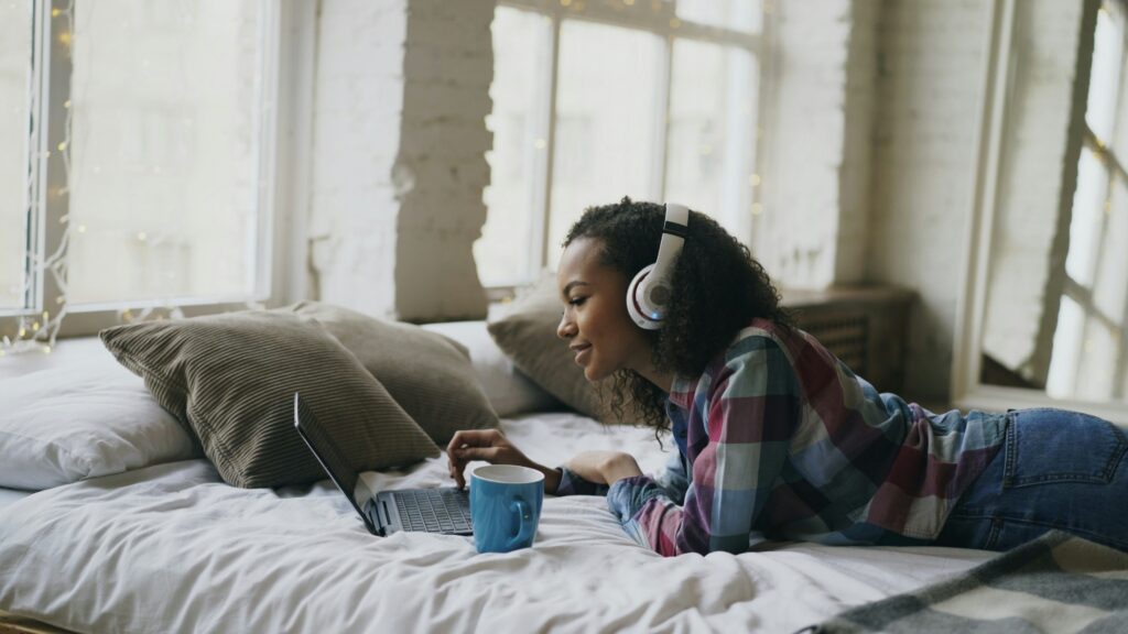 Teen practicing self-care and setting healthy boundaries for mental health while relaxing with laptop and headphones at home.