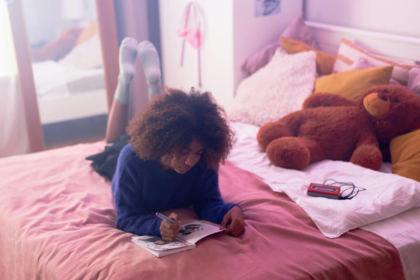 A teenage girl lying on her bed writing in a journal, practicing self-reflection and positive self-talk.
