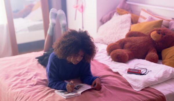 A teenage girl lying on her bed writing in a journal, practicing self-reflection and positive self-talk.