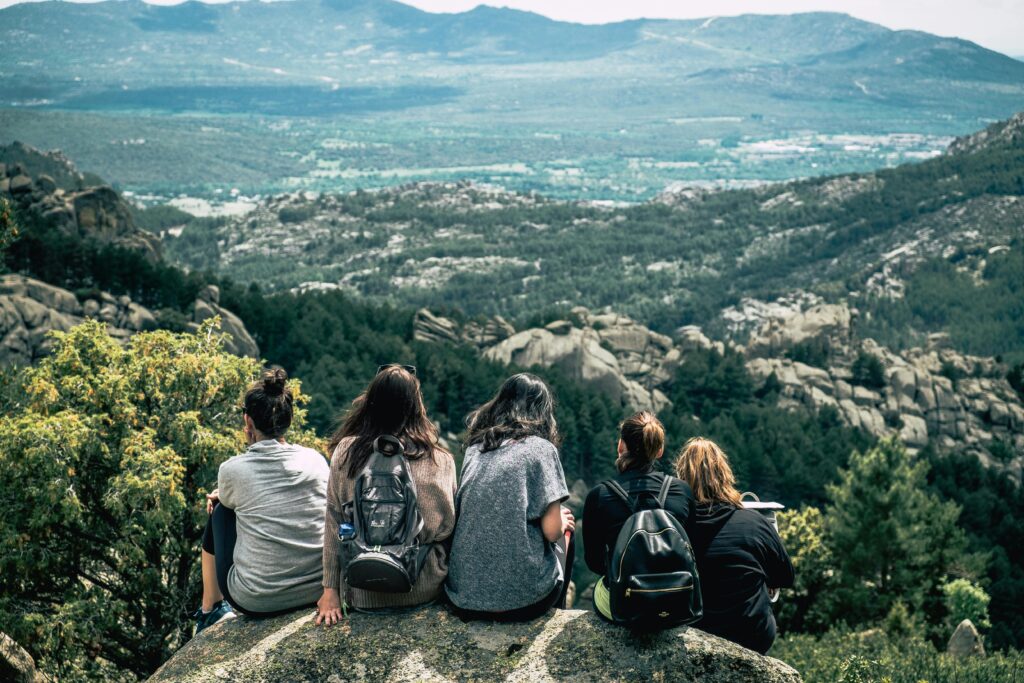 A group of young people sitting together on a rock overlooking a vast green mountain valley.