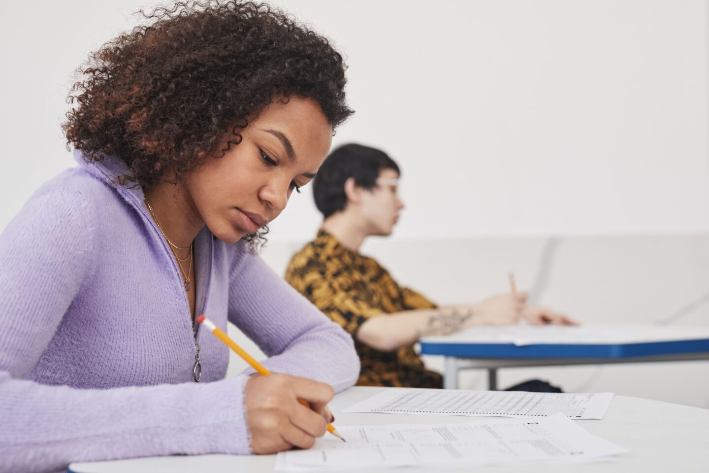 A teen in a purple sweater taking a test in a classroom.