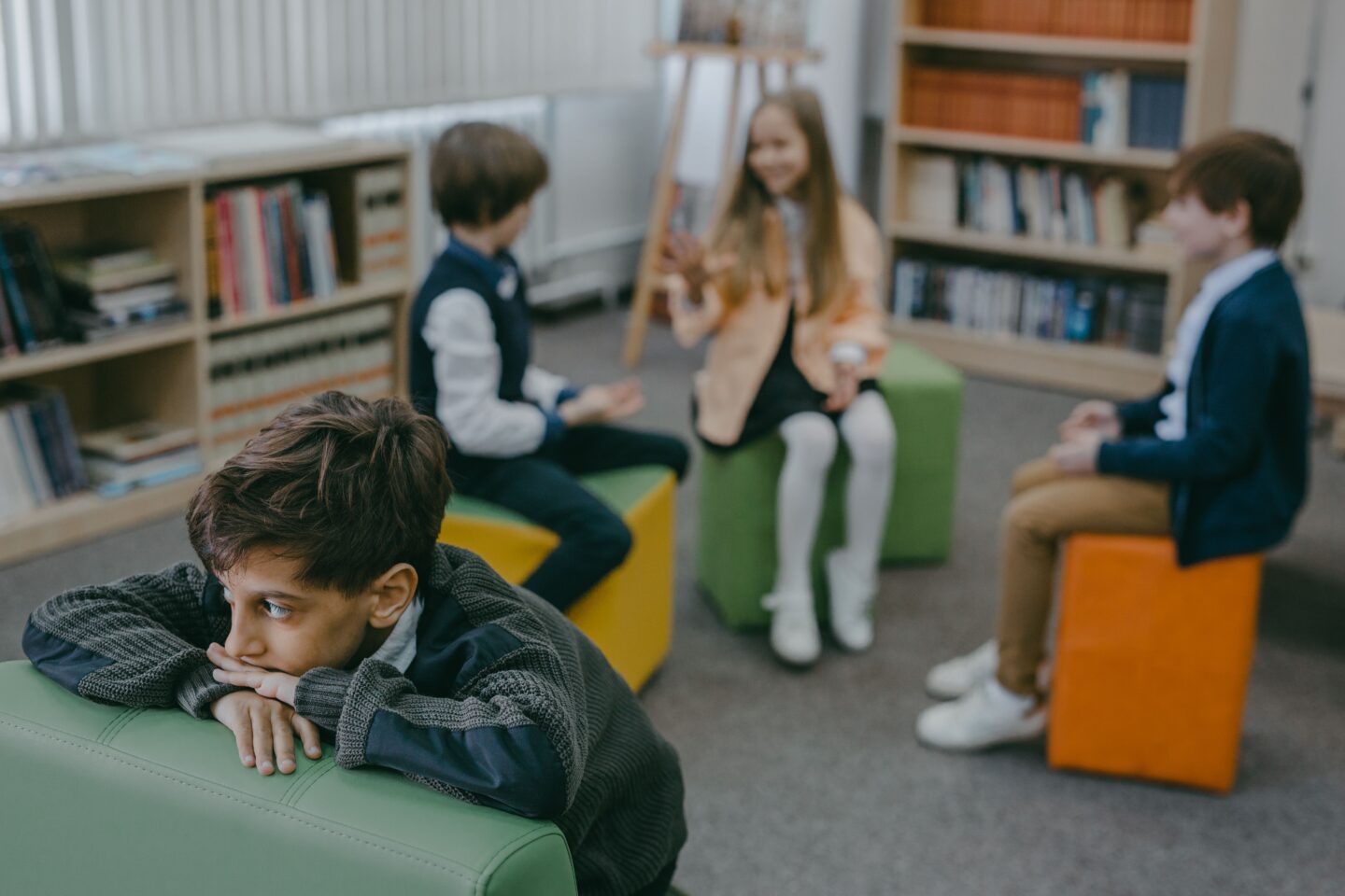 A boy sits apart from a group of classmates in a school library, illustrating how social anxiety can make connecting with others feel hard.