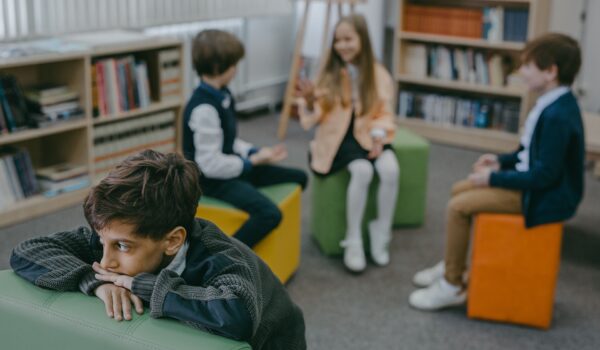 A boy sits apart from a group of classmates in a school library, illustrating how social anxiety can make connecting with others feel hard.