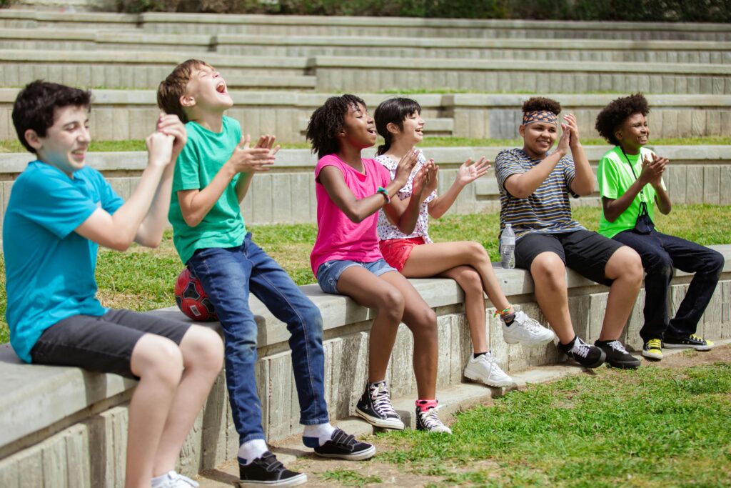 A group of smiling, laughing kids cheer together outdoors, showing the confidence and connection that comes from feeling at ease socially.