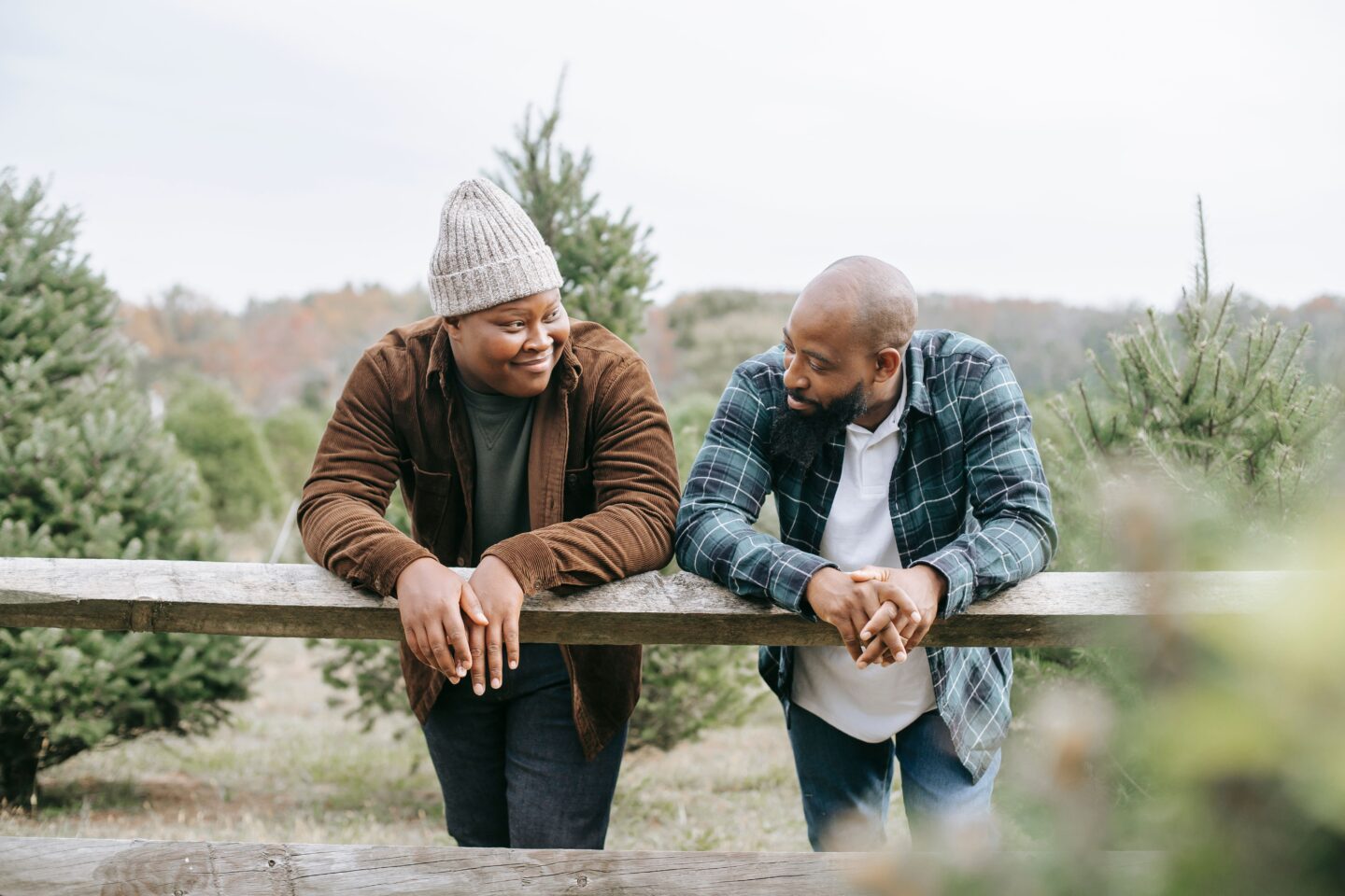 Father and son leaning on a wooden fence outdoors, smiling and talking with each other in a relaxed, supportive conversation.