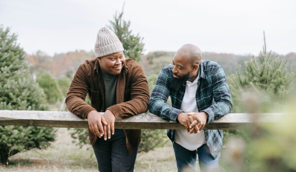 Father and son leaning on a wooden fence outdoors, smiling and talking with each other in a relaxed, supportive conversation.