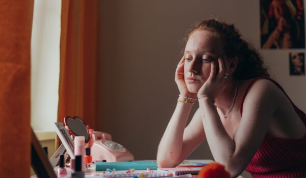 A teenager sitting at a desk, looking thoughtful, surrounded by schoolwork and an open journal.