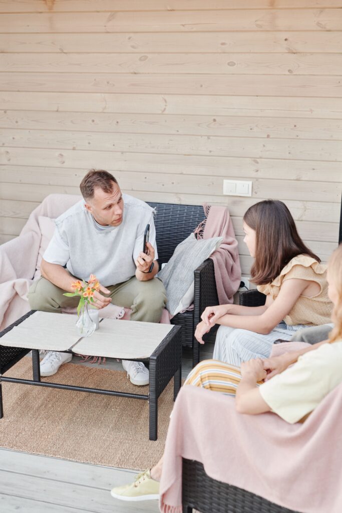 Family therapy session on a cozy porch, with a therapist showing something on his phone while a teenage girl and parent listen attentively.