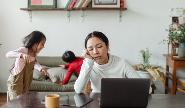 A tired parent sitting alone at a kitchen table with a cup of coffee, looking exhausted.